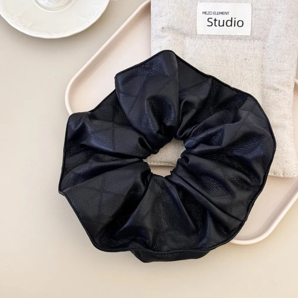Black quilted faux leather scrunchie with a ruffled edge.