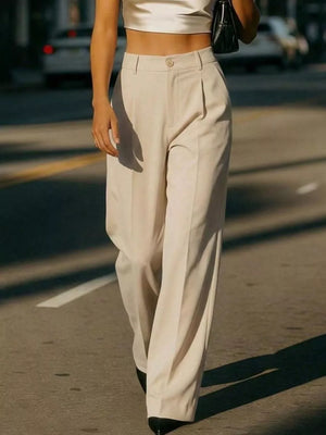 Cream high-waisted pleated trousers with a button closure, wide leg, and front pockets.