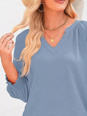 Light blue gray smocked long sleeve blouse with V-neck and textured polyester fabric.