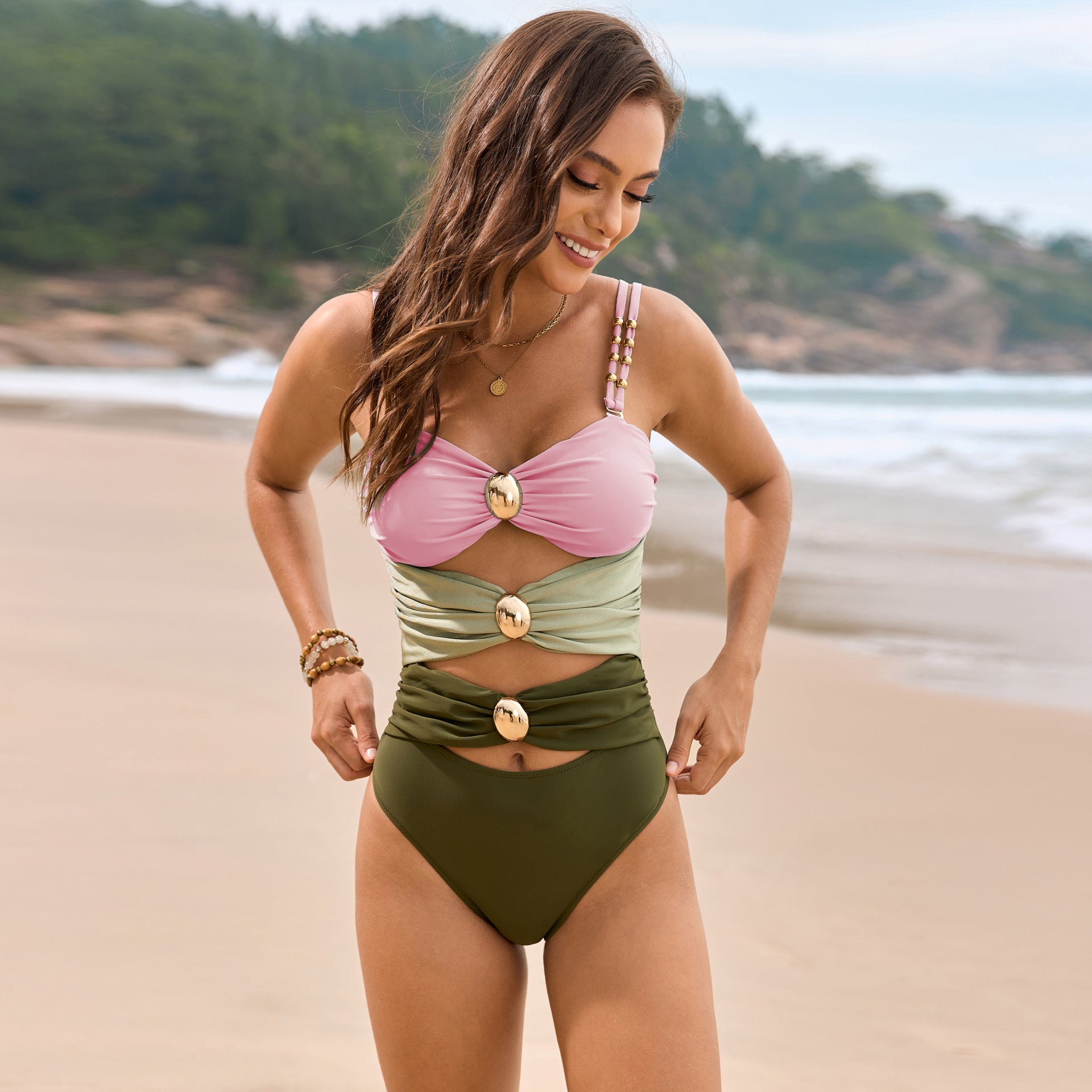 Colorblock one-piece swimsuit with gold hardware details and cutouts in blush pink, sage green, and olive.