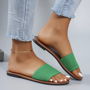 Green perforated comfort slide sandals with brown sole and casual frayed jeans.