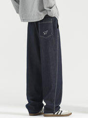 Men's dark wash wide-leg jeans with white stitching and paper airplane pocket detail.