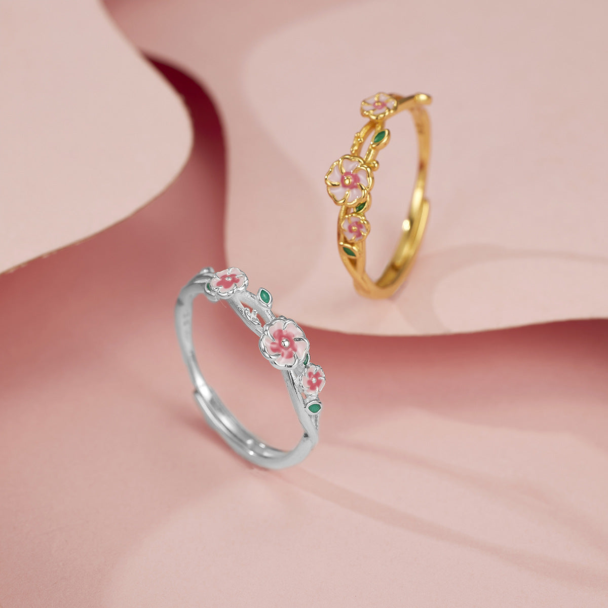 Delicate flower-inspired sterling silver ring in gold and silver, featuring pink blossoms and green leaves.