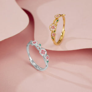 Delicate flower-inspired sterling silver ring in gold and silver, featuring pink blossoms and green leaves.