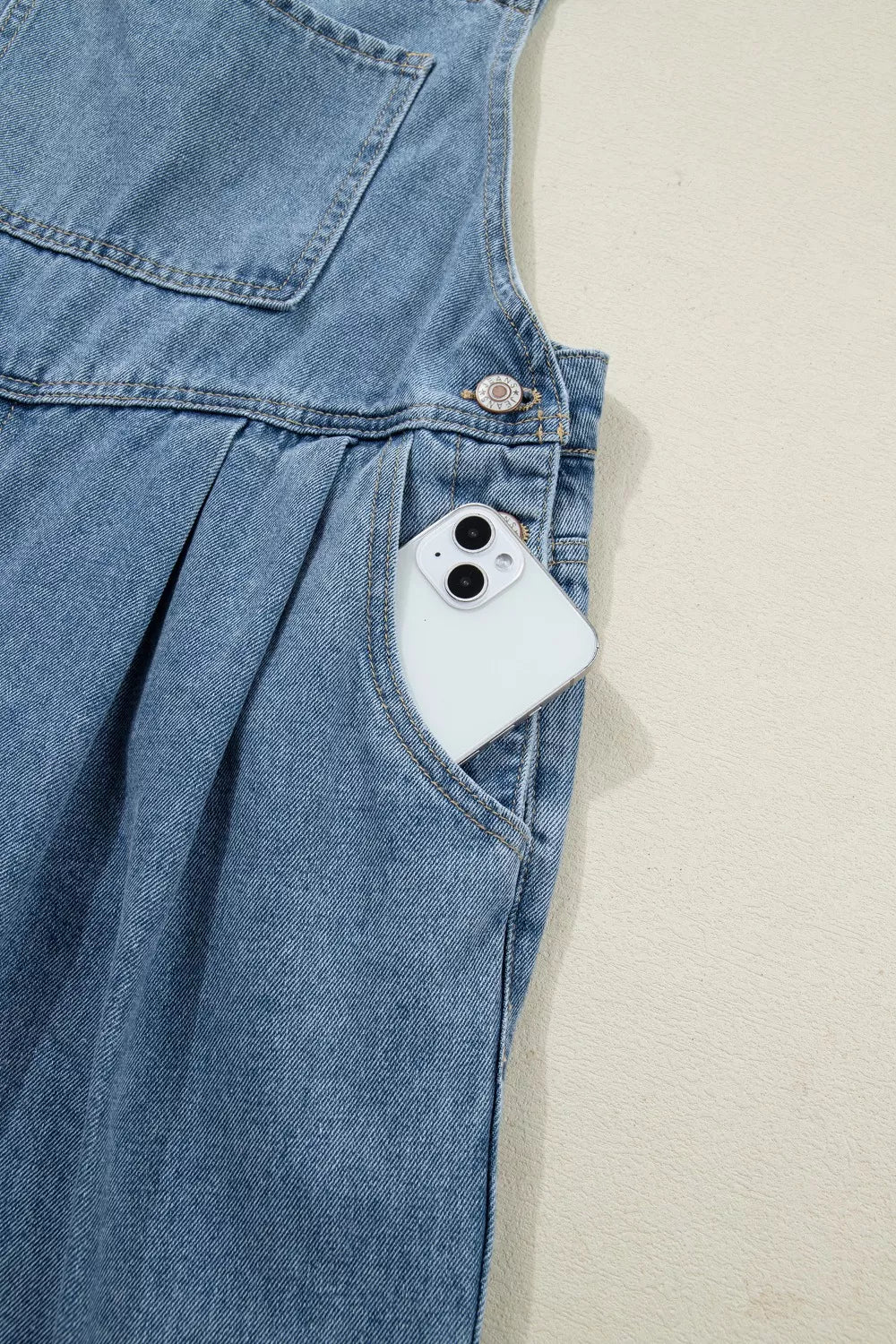 Denim jumpsuit with wide legs, pleats, and a pocket holding a smartphone.