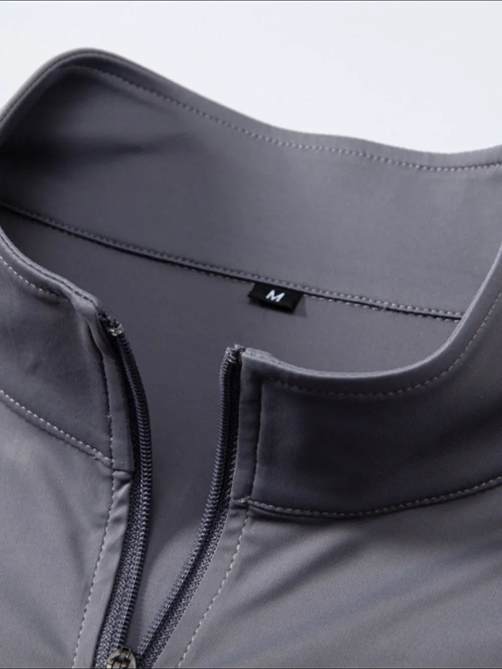Performance zip-neck tee in dark gray with structured shoulders and a size M tag.