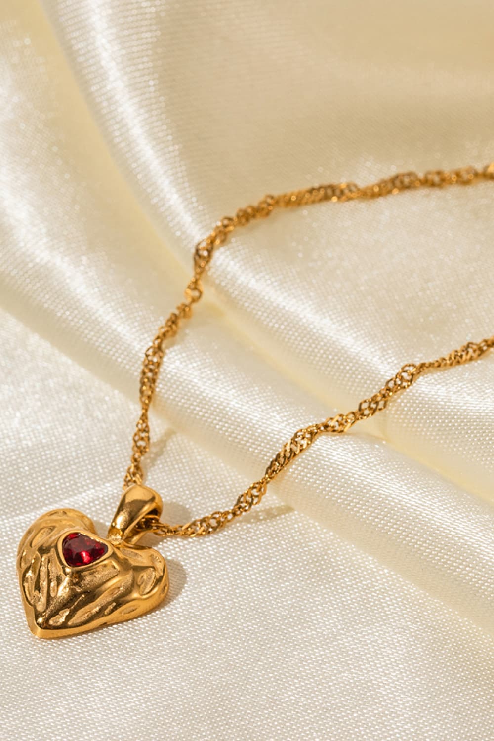 Textured gold heart pendant necklace with red stone on a delicate chain.