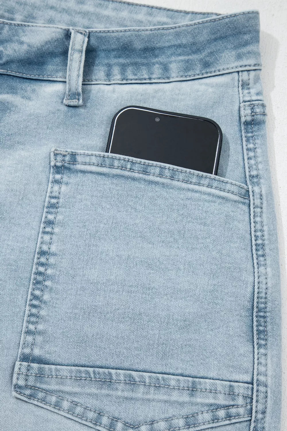 Light wash denim jeans with raw hem and utility pocket detail, showing a phone.
