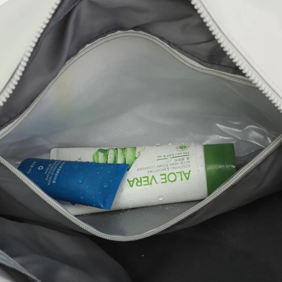Interior view of a white duffle bag showing Aloe Vera cleanser and blue cream.