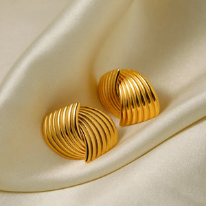 Sculpted gold coil earrings with ribbed texture on satin fabric