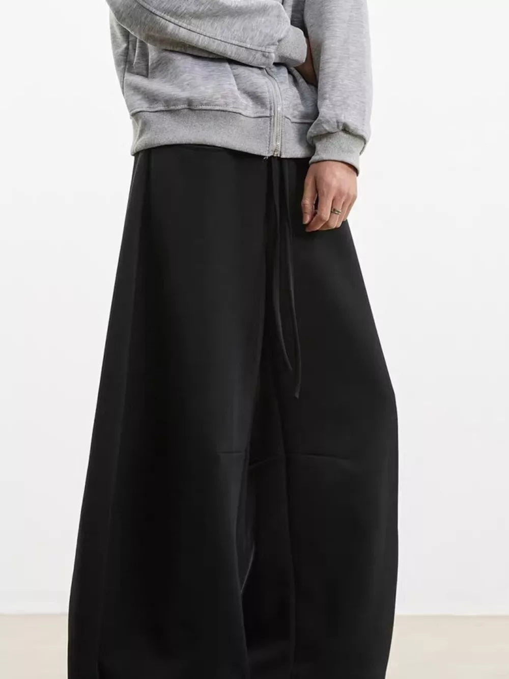 Black wide-leg sweatpants with drawstring waist, shown with a grey zip-up hoodie.