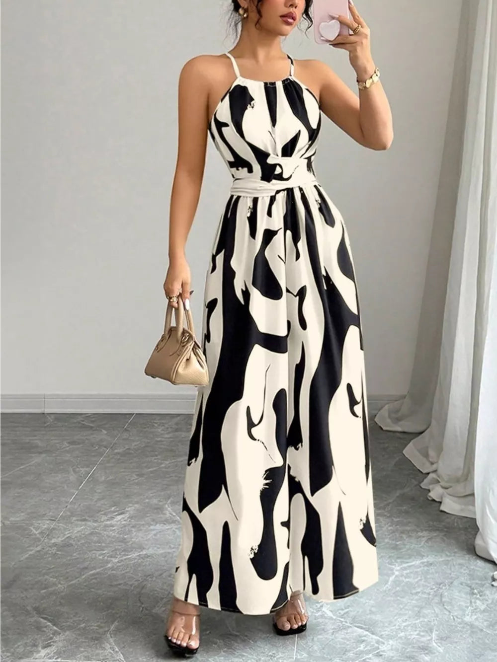 Chic halter neck maxi dress in white with abstract black print, featuring a belted waist.