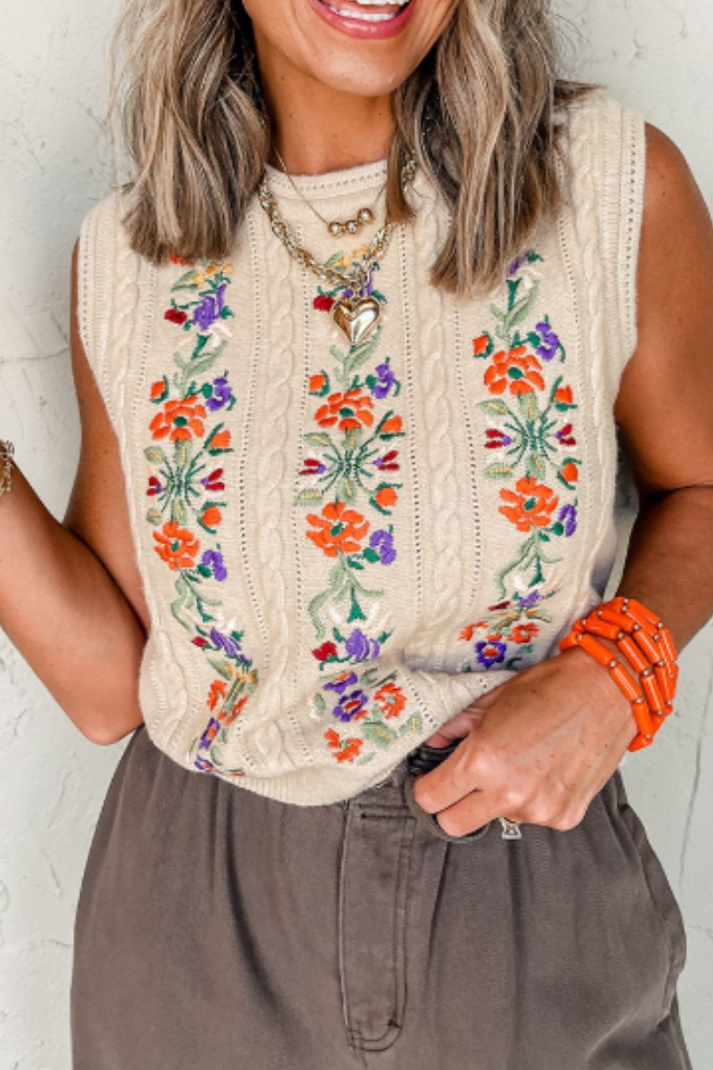 Beige cable knit vest with floral embroidery and a crew neckline.