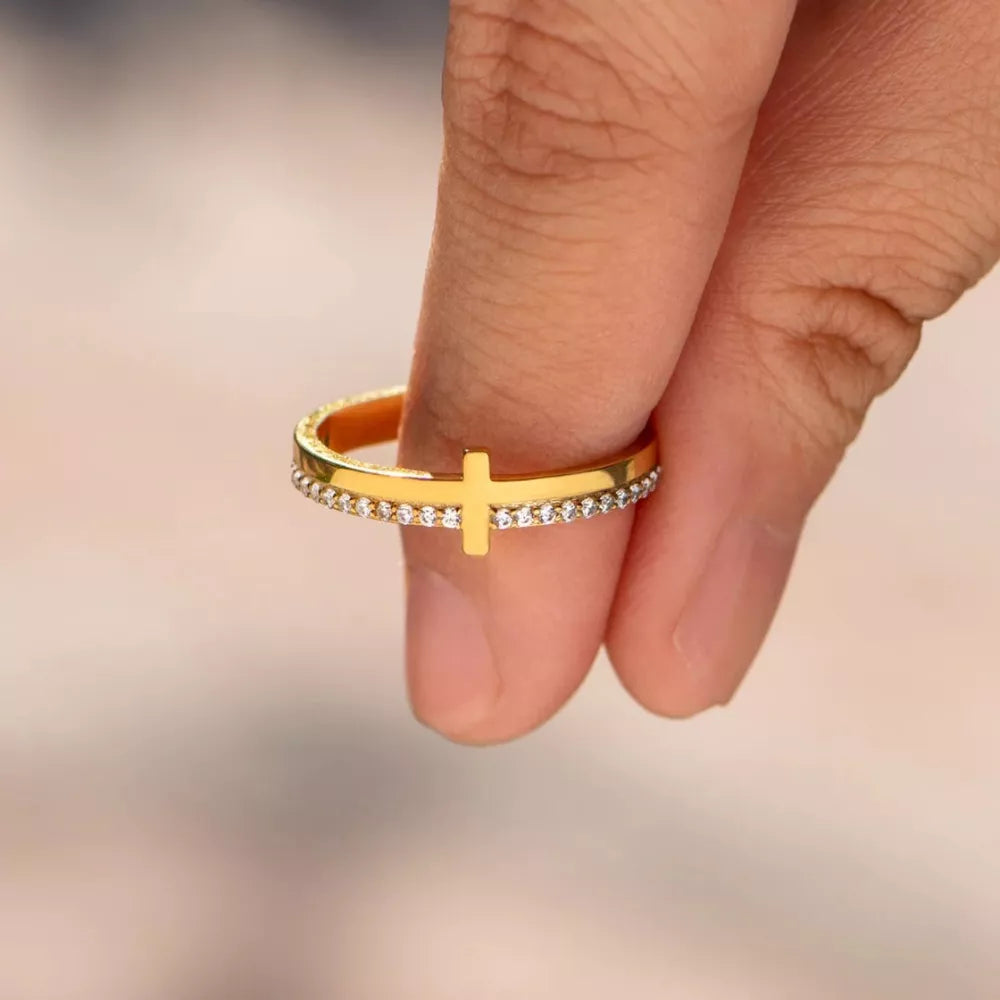 Gold-plated ring with a cross detail and small stones on the band.