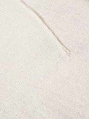 Cream knit sweater detail with textured stitching and abstract pattern.