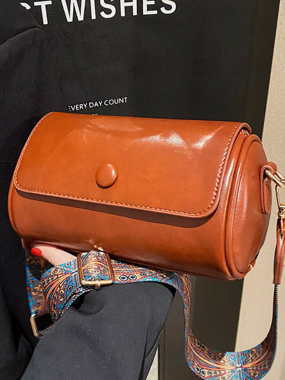 Brown leather crossbody bag with ethnic patterned strap and gold buckle.