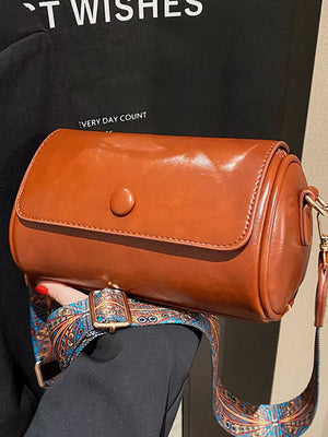 Brown leather crossbody bag with ethnic patterned strap and gold buckle.