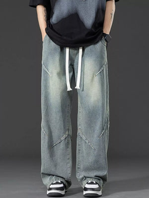 Men's vintage-inspired oversized blue denim jeans with white drawstring and unique seam details.