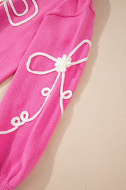 Fuchsia pink knit sweater with white embroidered bow motif and playful swirls.