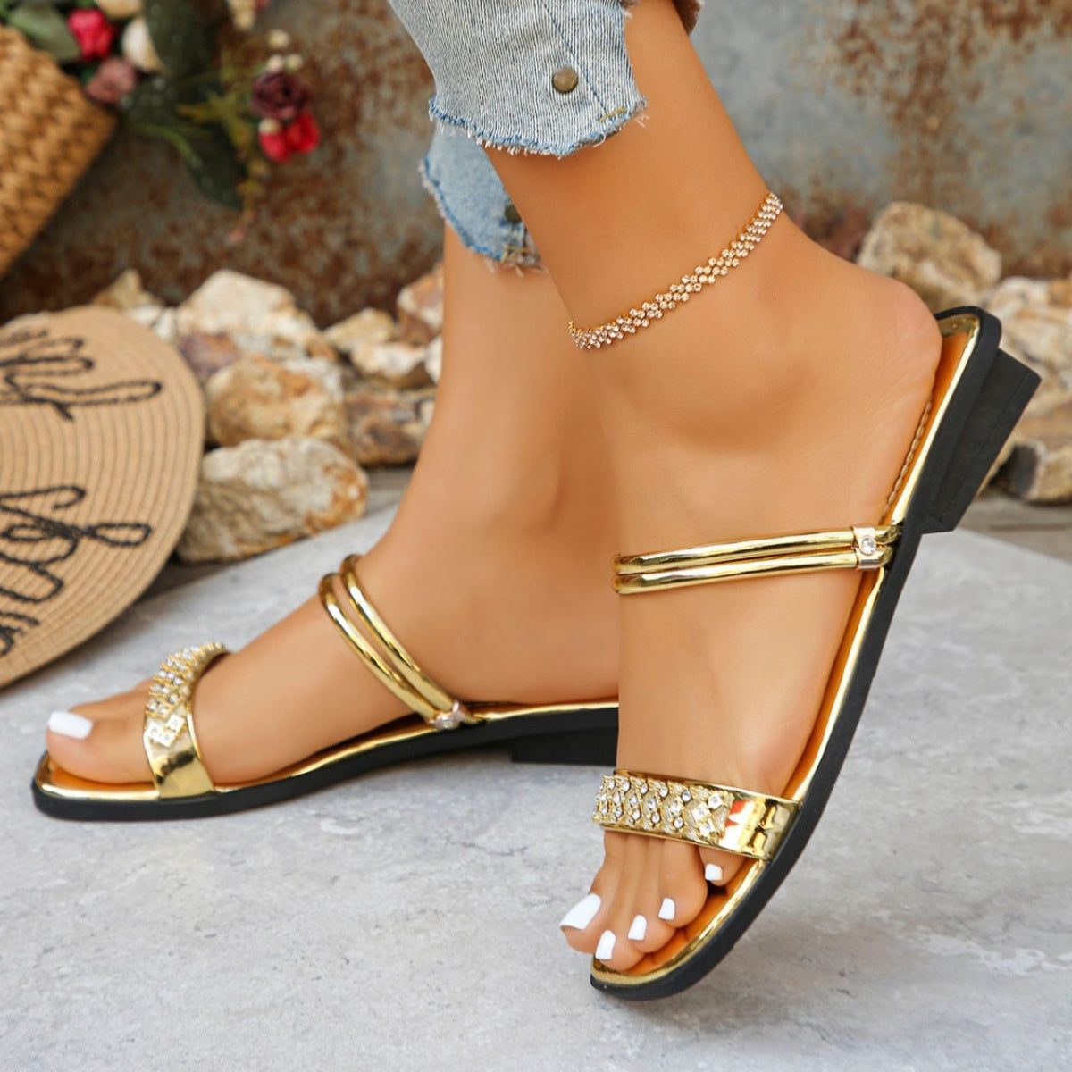 Gold flat sandals with double straps and rhinestone embellishments on the toe strap.