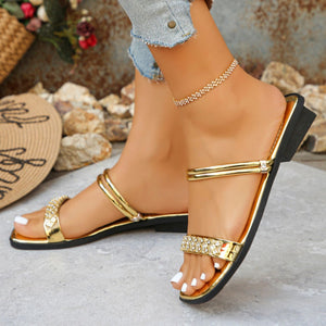 Gold flat sandals with double straps and rhinestone embellishments on the toe strap.