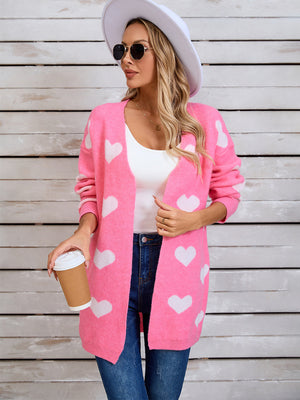 Pink acrylic cardigan with white intarsia hearts, open front, long sleeves.