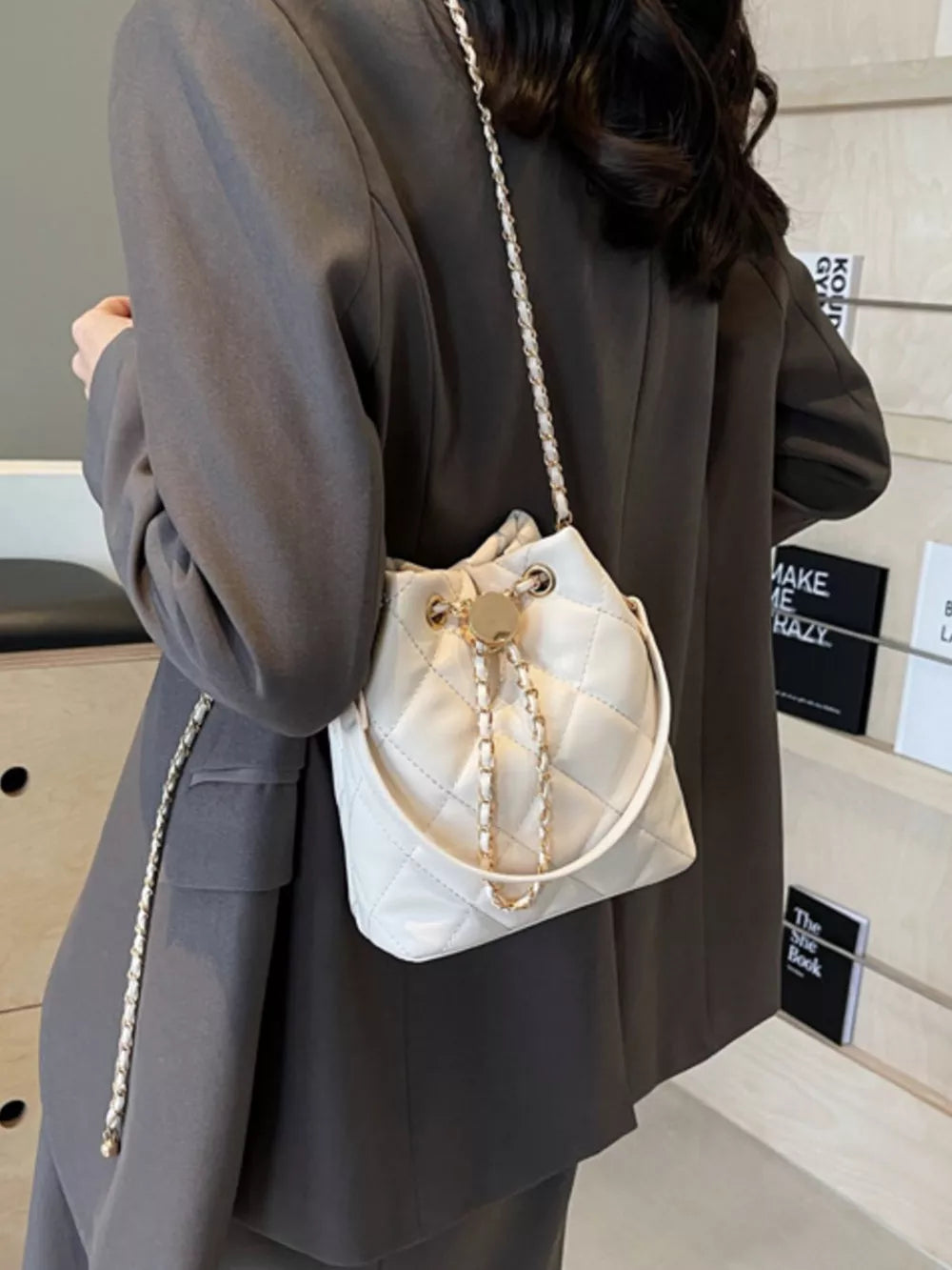 White quilted bucket bag with gold chain strap and drawstring closure.