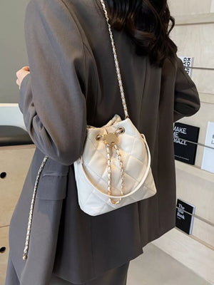 White quilted bucket bag with gold chain strap and drawstring closure.