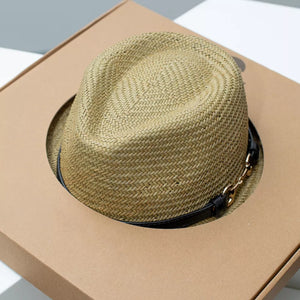 Woven straw fedora hat in natural with black decorative band and gold chain detail.