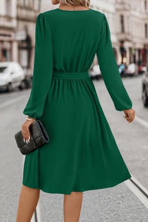Emerald green midi dress with poet sleeves, belted waist, and a flowing skirt.
