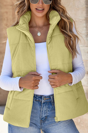 Corduroy padded vest in sage with a high collar and zip front, styled with a white long-sleeve top.