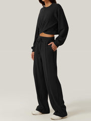 Black cross-front knit lounge top with crew neck and long sleeves, paired with wide-leg sweatpants.