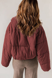 Cropped puffer jacket in brick red with a hooded collar and horizontal quilting.