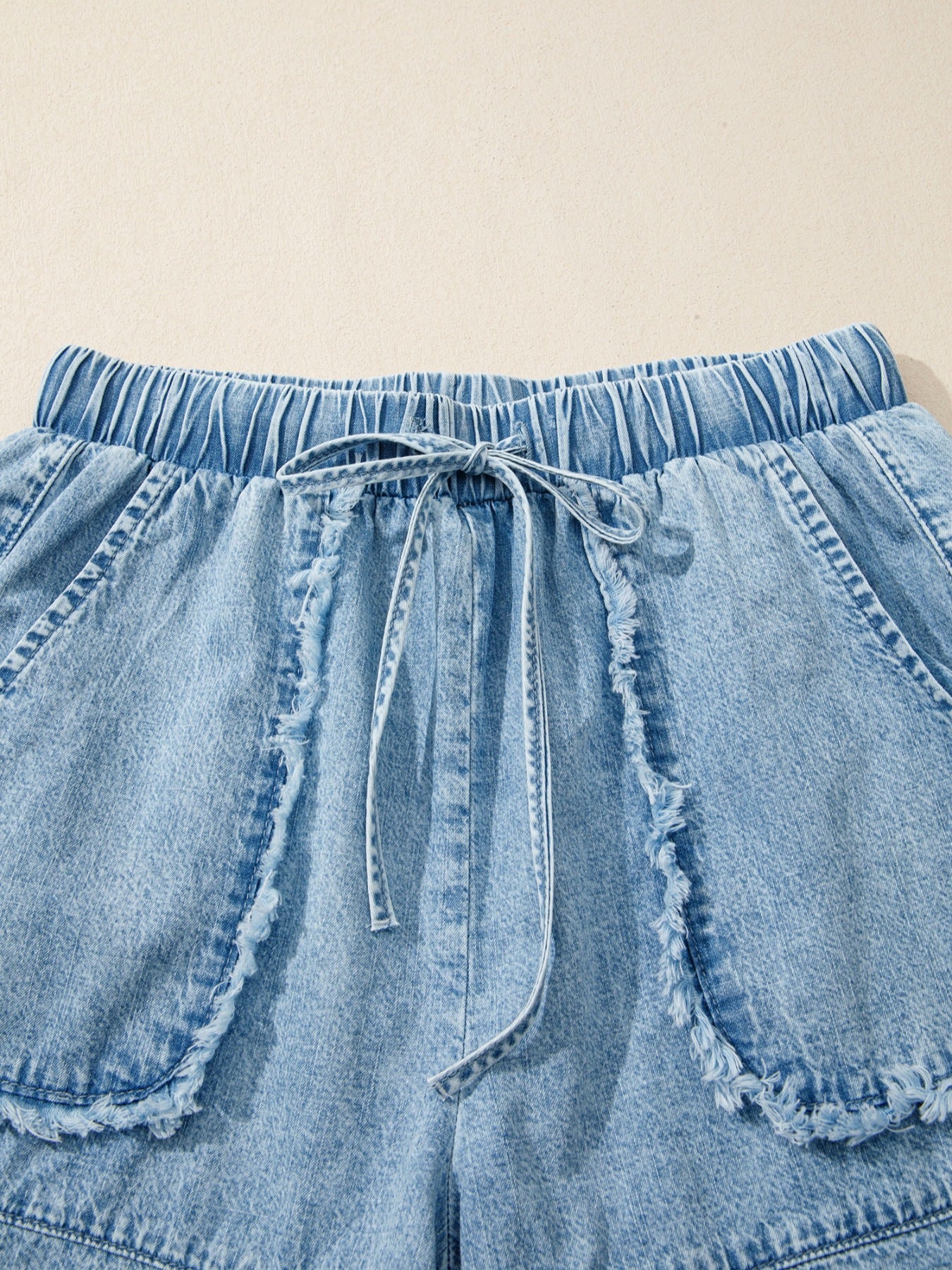 Light wash denim shorts with elastic drawstring waist and frayed pocket details.