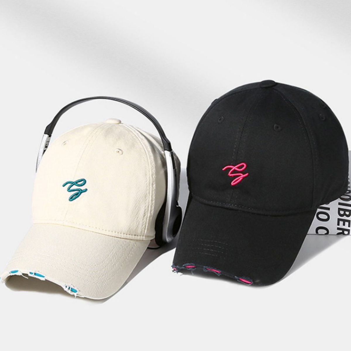 Distressed cotton baseball caps in off-white and black with embroidered logos and frayed details.