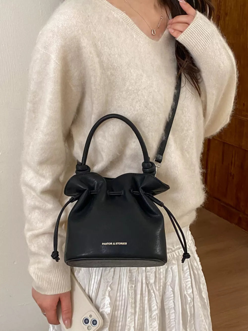 Black pu leather cinch-top crossbody bag with drawstring and knotted handles.
