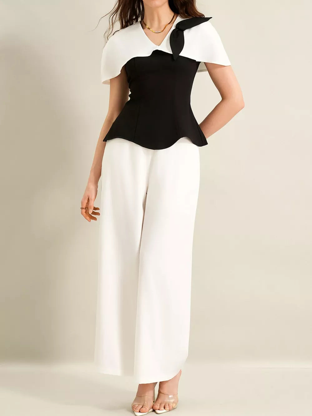 Black peplum top with white cape sleeves and bow detail, paired with white wide-leg pants.