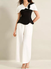 Black peplum top with white cape sleeves and bow detail, paired with white wide-leg pants.
