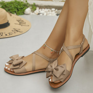 Khaki crisscross bow sandals with ankle straps and a flat sole.
