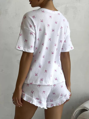 White ribbed knit pajama set with pink bow print, featuring a cropped t-shirt and ruffled shorts.