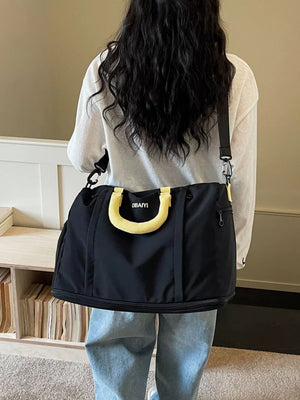 Black nylon travel duffel bag with yellow padded handle and adjustable strap.