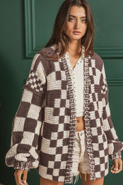 Chic checkered acrylic cardigan with balloon sleeves and open front, styled with a white top and shorts.