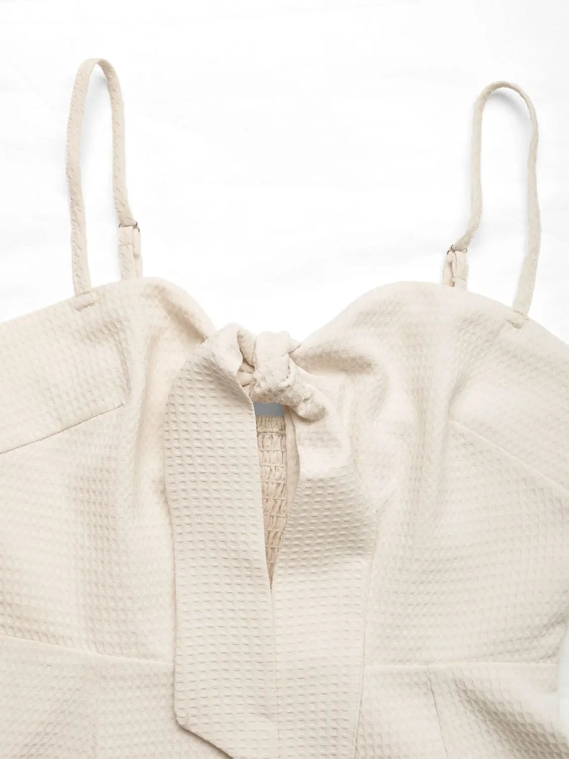 Beige textured romper with tie-front detail and smocked bodice.