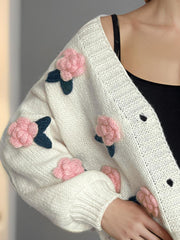 White knit cardigan with pink embroidered rose appliqués and dark green leaves.