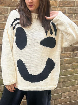 Cream knit sweater with abstract black smiley face graphic, crew neck, long sleeves.