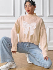 Blush pink turtleneck knit sweater with white lace bow appliqué detail.