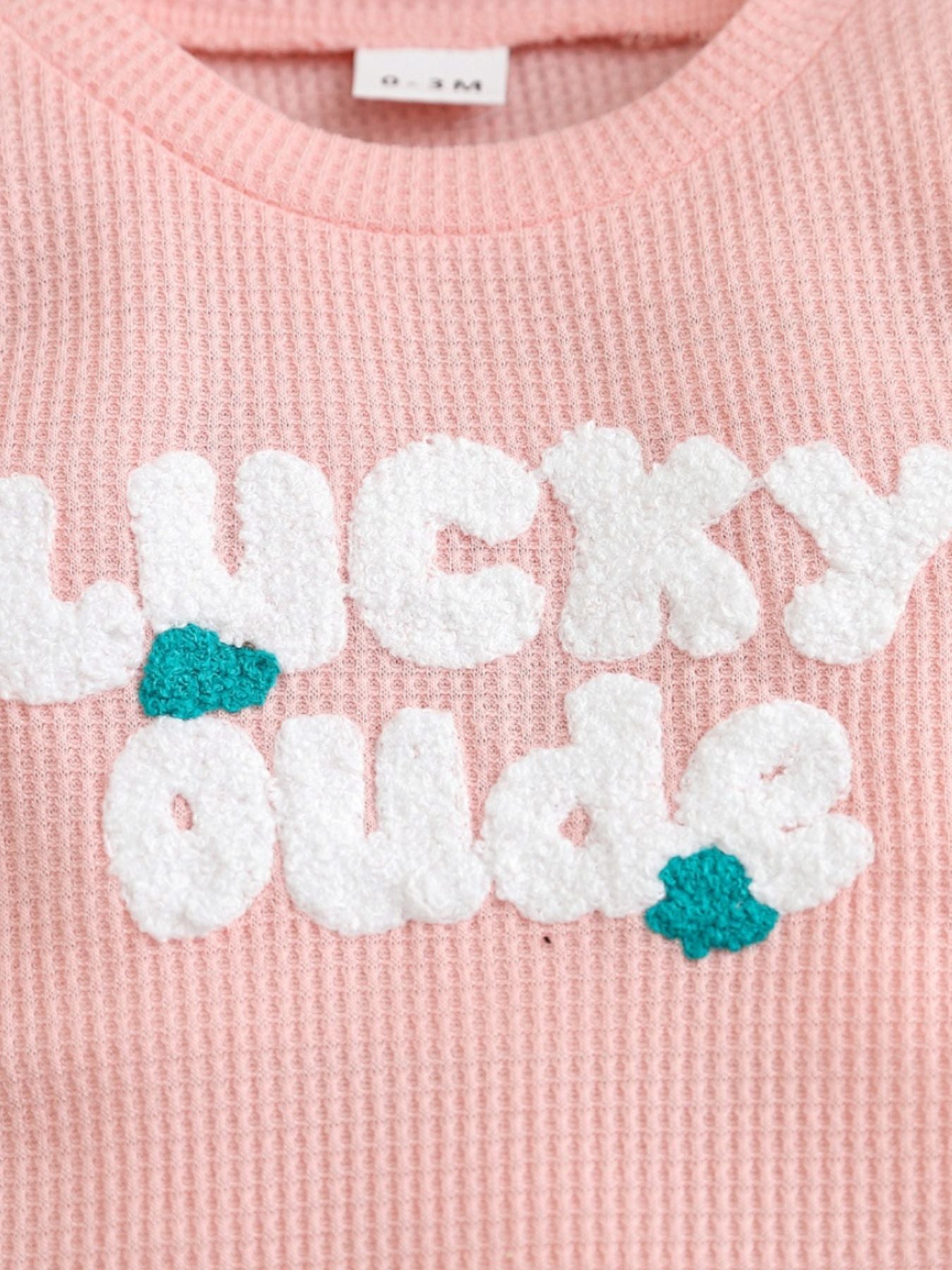Pink waffle knit baby one-piece with textured white Lucky Dude lettering and teal accents.