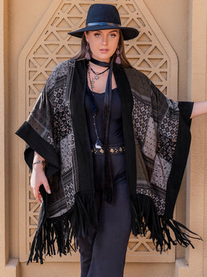 Black patchwork print kimono with fringe and wide sleeves, styled with a hat and jewelry.