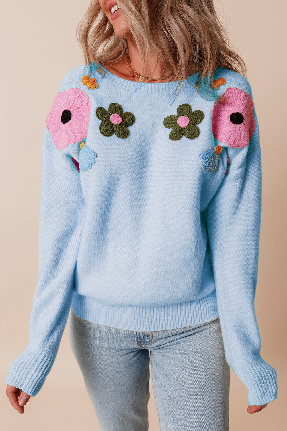 Light blue knit sweater with embroidered floral appliqué details and ribbed cuffs.