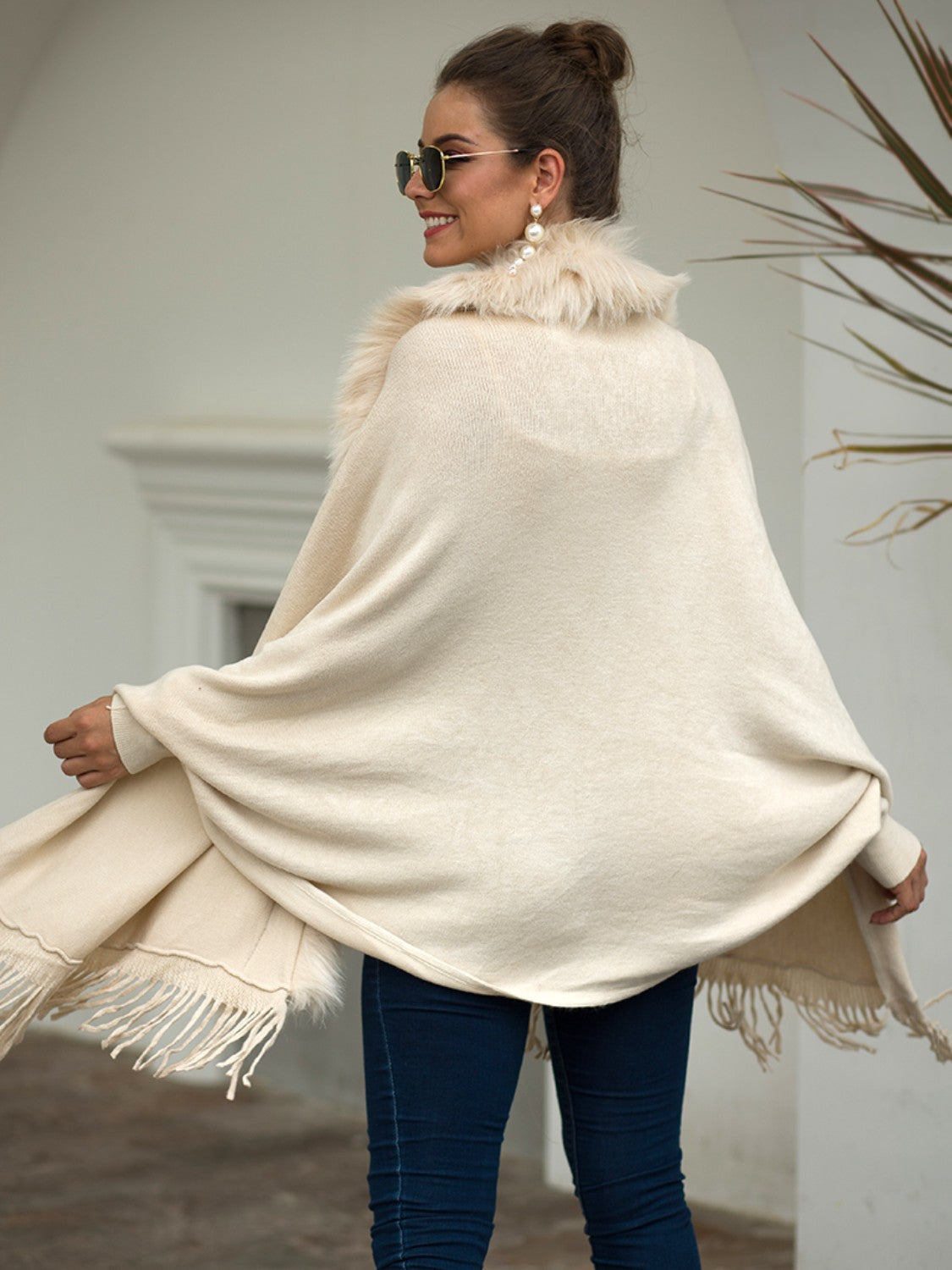 Ivory knit cape with faux fur trim and fringe detailing.
